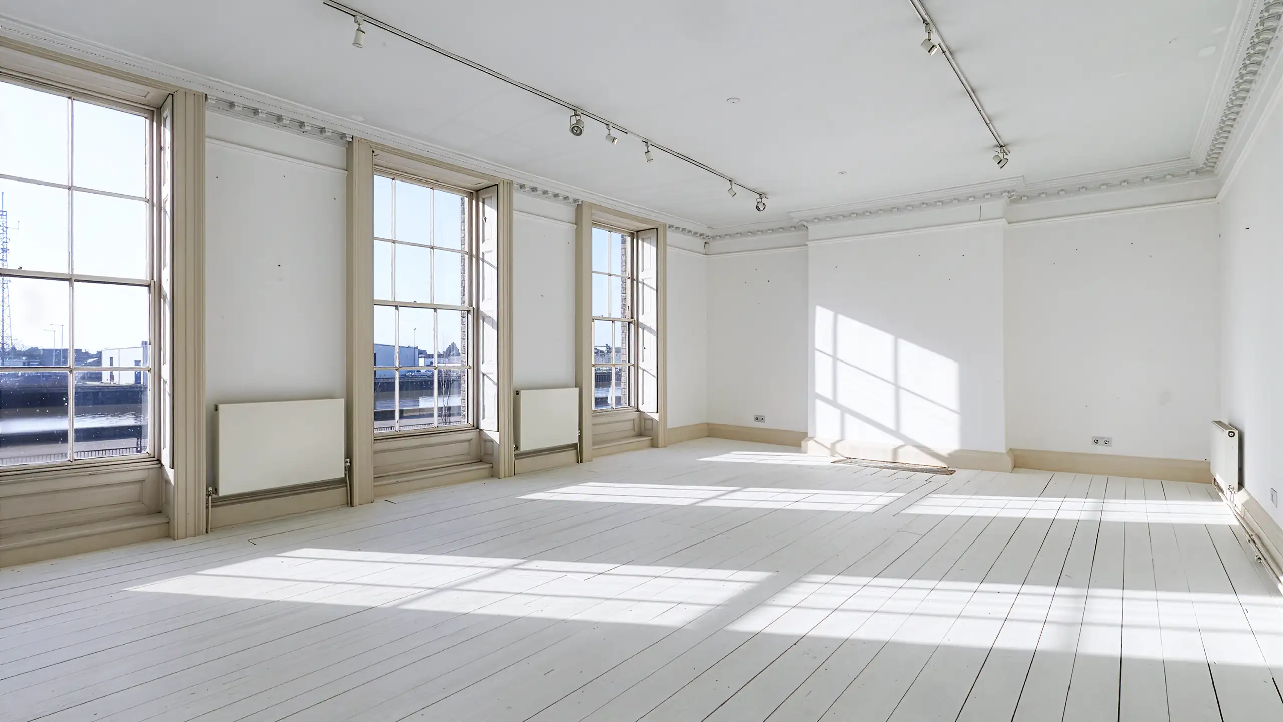 A large, open-plan studio space with multiple windows, white walls, and various tables and chairs set up for a workshop or meeting.