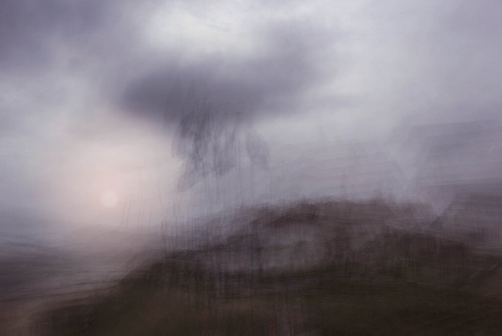 A long exposure photo of a dark, blurry landscape with a hazy sun in the distance under a cloudy sky